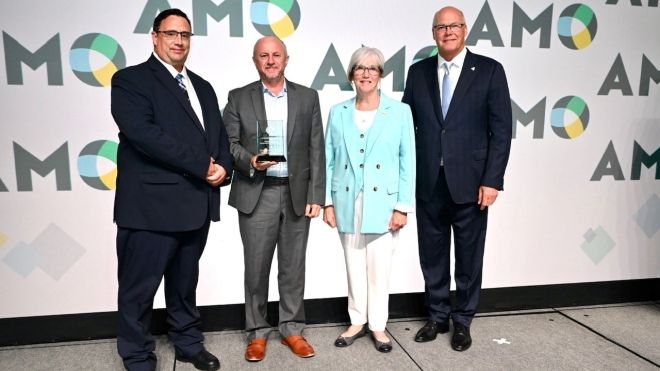 Image of four individuals set against AMO backdrop with one individual holding an award