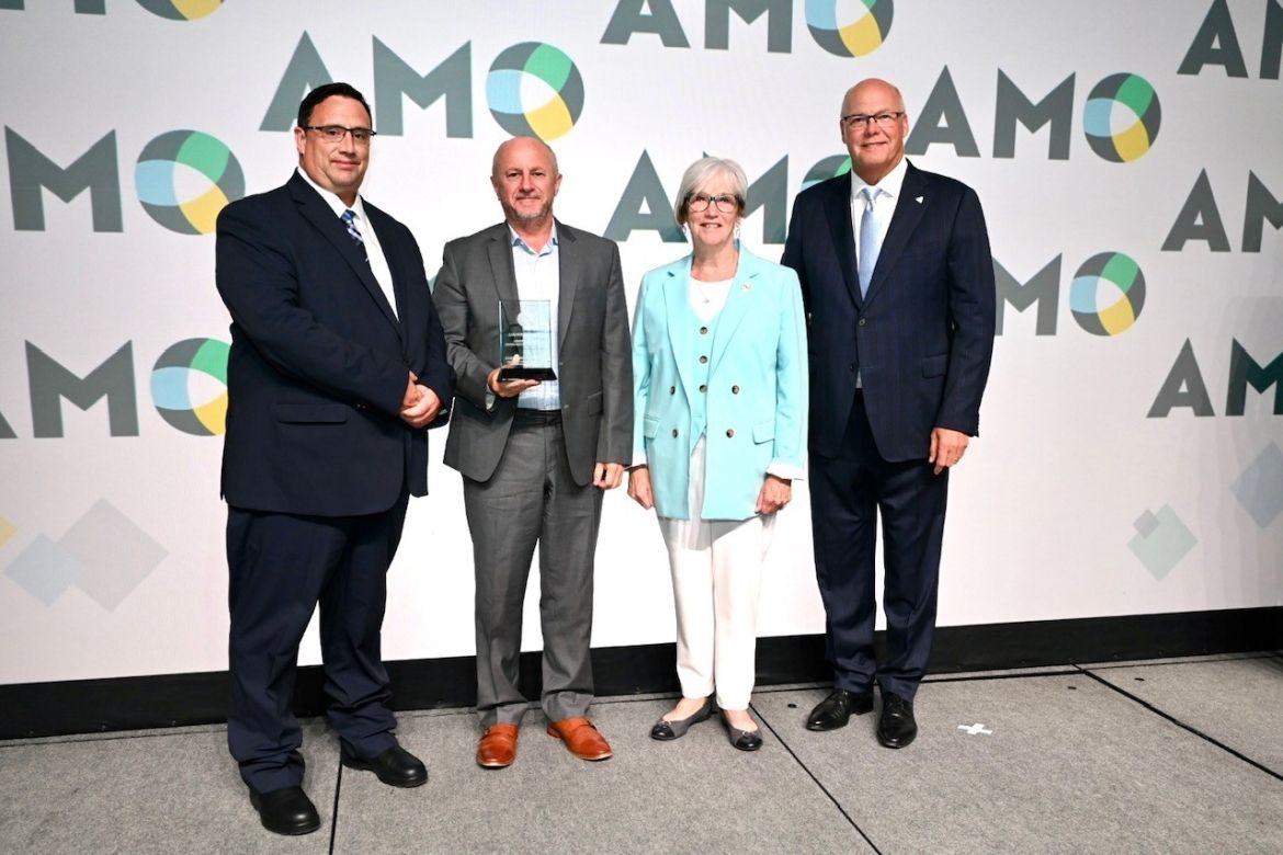 Image of four individuals set against AMO backdrop with one individual holding an award